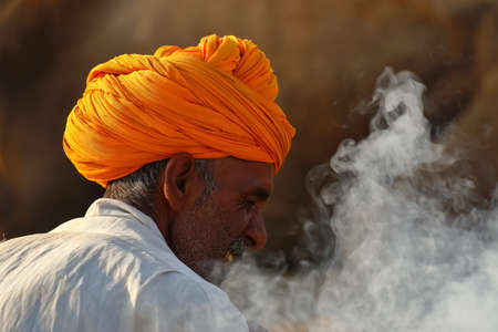 A Selective focus Abstract side portrait of a Rajasthani man wearing an orange turban with smoke around him in Pushkar, Rajasthan India on 29 October 2017のeditorial素材