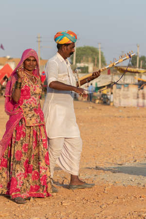 Selective focus image of a man along with a women dressed in traditional rajasthani clothes playing musical instrument violin at Pushkar festival at Pushkar, Rajasthan, India on 19 November 2018のeditorial素材