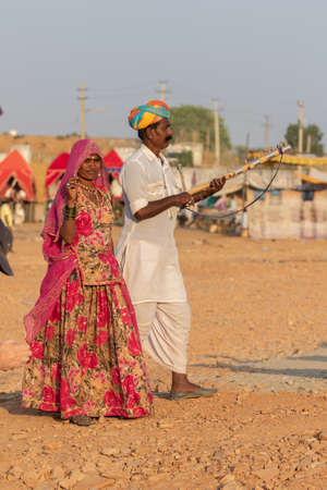 Selective focus image of a man along with a women dressed in traditional rajasthani clothes playing musical instrument violin at Pushkar festival at Pushkar, Rajasthan, India on 19 November 2018のeditorial素材