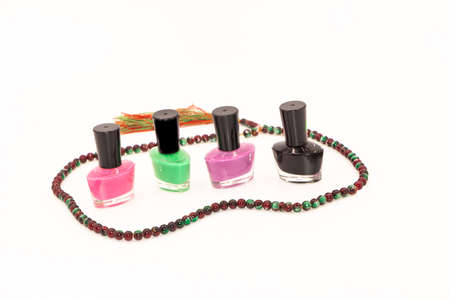 Selective focus image of Nail polish bottles of different colors and a beautiful necklace around it with white backgroundの写真素材