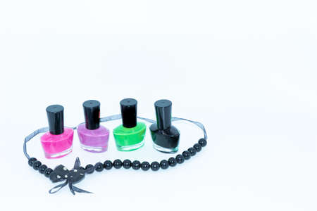 Selective focus image of Nail polish bottles of different colors and a beautiful necklace around it with white backgroundの写真素材
