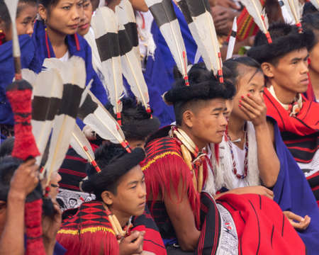 Selective focus image of young Naga boys and girls siting together wearing colorful attire and shawls in Kisama Heritage village in Nagaland India on 3 December 2016のeditorial素材