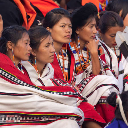 Selective focus image of young Naga tribeswomen siting together wearing colorful attire and shawls in Kisama Heritage village in Nagaland India on 3 December 2016のeditorial素材