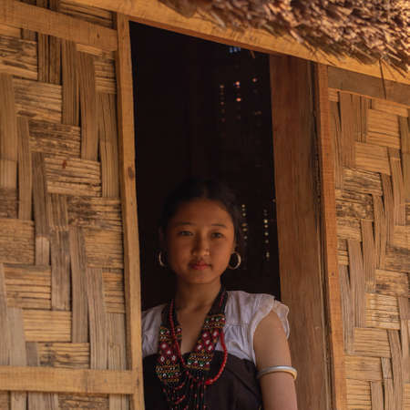 Portrait of a young tribal Naga women dressed in traditional attire looking out of the window of a...