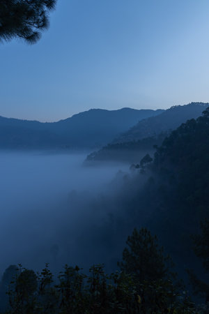 Layers of mountains with pine trees on them and fog and mist  settled in the valley