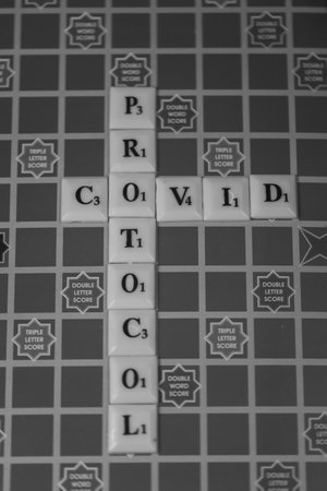 Selective focus image of alphabets on square coins used to depict the the word COVID PROTOCOL