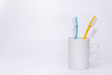 A pair of colourful tooth brusher kept inside a withe cup with white  copy space backgroundの写真素材