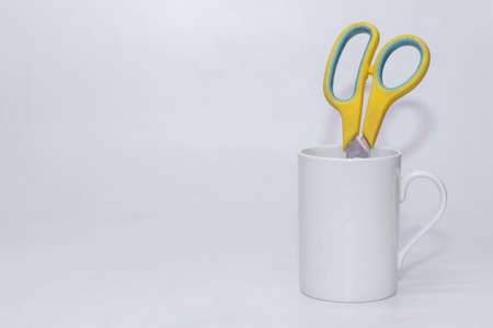 A yellow colored Scissor isolated kept inside a white cup with plain white background and copy space