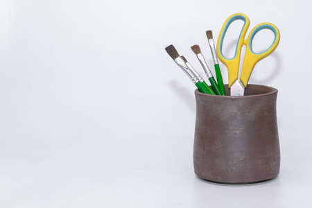 Green colored paint brushes and a yellow scissors kept inside a dark brown stationery holderの写真素材