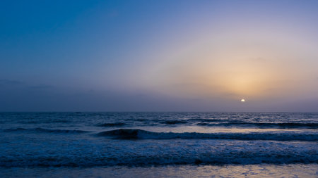 A view of the sky with sun setting in the horizon and waves in the oceanの写真素材