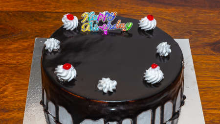 A dark chocolate cake with fresh white cream and cherry topping and Happy birthday written on itの写真素材