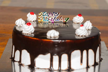 A dark chocolate cake with fresh white cream and cherry topping and Happy birthday written on itの写真素材