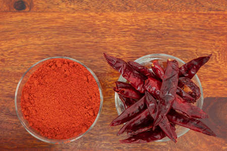 Top view of dry red chillies and red chilli powder bowls kept side by side