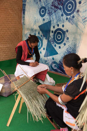 Nagamese women weaving  strands of dry grass together with hands to make traditional Indian...
