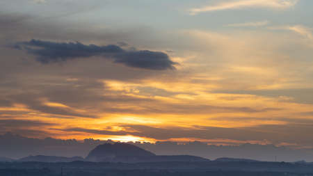 Silhouette of a hill against beautiful golden hour light and beautiful clouds formation in the horizon with the sun settingの写真素材