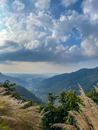 View of cloud formation, mountain ranges  and river flowing in the background and dry grass in the foregroundの写真素材