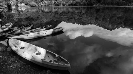 Boats on the shore of a lake with the reflection of sky and hills falling on waterの写真素材