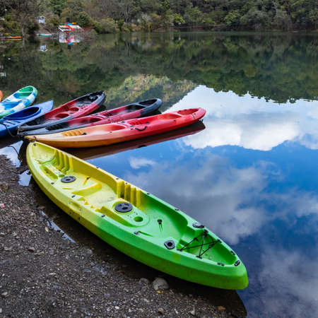 Colorful boats on the shore of a lake with the reflection of sky and hillsの写真素材