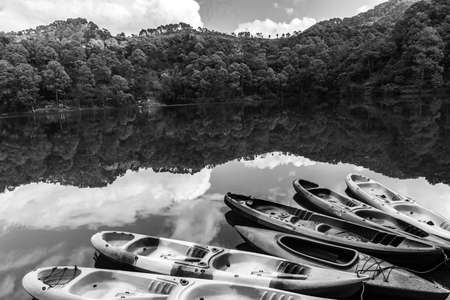 Boats on the shore of a lake with the reflection of sky and hills falling on waterの写真素材