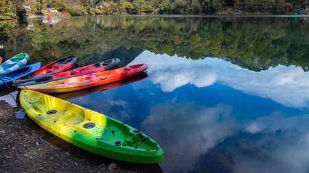 Colorful boats on the shore of a lake with the reflection of sky and hillsの写真素材
