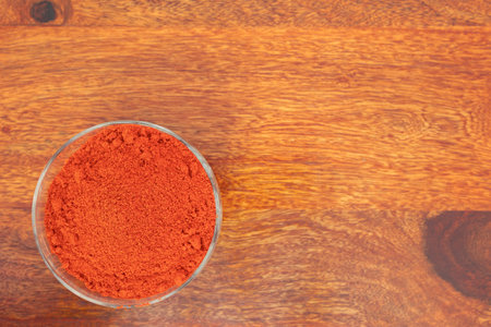 Paprika powder in glass bowl on wooden background, top viewの写真素材