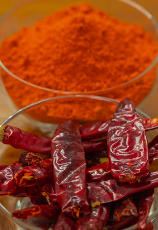Dried red hot chili peppers in glass bowl and powder on tableの写真素材