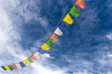 Colorful Tibetan prayer flags attached to a string flying in air against blue sky with cloudsの写真素材