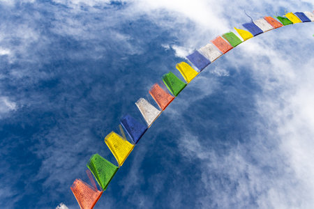 Colorful Tibetan prayer flags attached to a string flying in air against blue sky with cloudsの写真素材