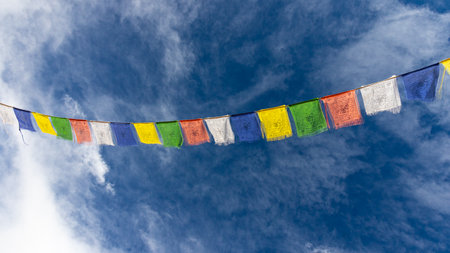 Colorful Tibetan prayer flags attached to a string flying in air against blue sky with clouds