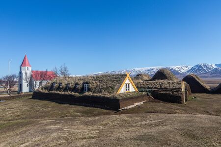 Historic turf-roofed farmhouses built with peat. The sod houses are flanked by a church while the background shows the mountain range around Olafsfjordur. Glaumbaer, Varmahlid, Icelandの写真素材
