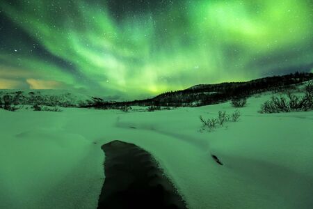 Northern lights Aurora Borealis in the night. A little water stream on the foreground with a artic, snowy winter landscape.の写真素材