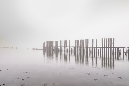 Old wooden groyne on a coastline with heavy dense fog with low visibility during a cold Winter morning. The horizon is not visible.の写真素材