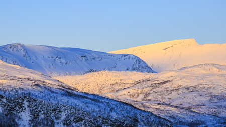 Close-up view on snowy mountain peaks at a scandinavian fjord during a winter sunsetの写真素材