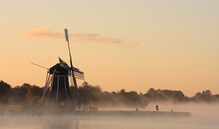 Cyclist by traditional Dutch windmill in a foggy sunrise の写真素材
