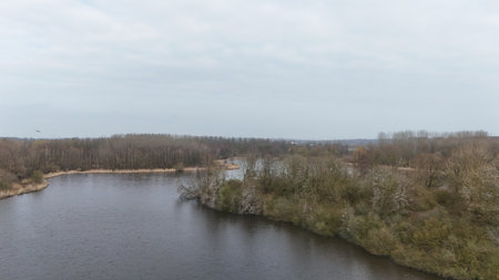 Serene river landscape with bare trees on a cloudy day, depicting a tranquil natural scene suitable for backgrounds or environmental themes.の写真素材