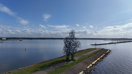 Scenic view of a large metal sculpture by a calm lake with a clear blue sky overhead, featuring a...