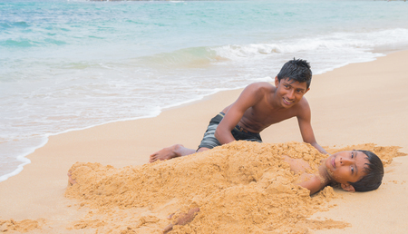 Two boys play in the sand on the ocean.のeditorial素材