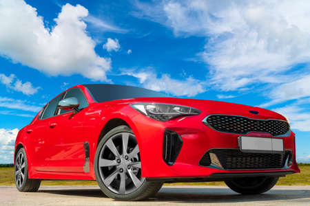 Red car on a blue sky background with white clouds. A stylish, modern, bright image of an avto mobile for design solutions.の写真素材
