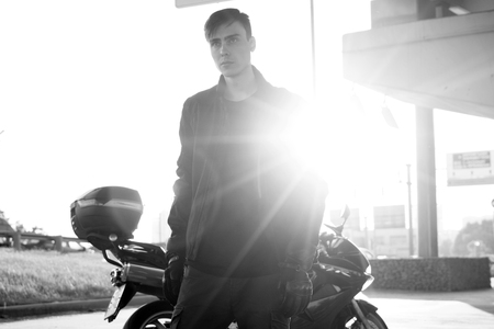 A white young man is standing next to a motorcycle.の写真素材