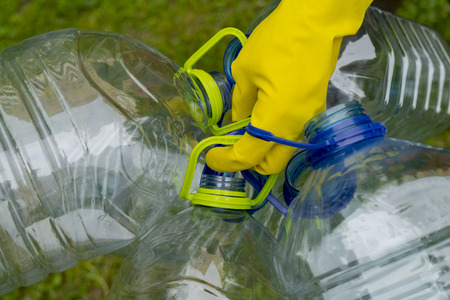 Garbage collection. Hand in yellow glove holding big empty plastic bottles. Grass on a background.の写真素材