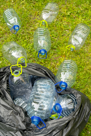 Plastic bottles in a black plastic trash bag on a grass background.の写真素材