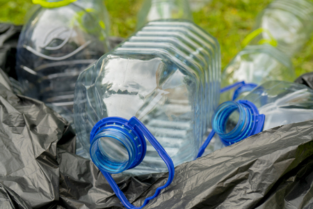 Plastic bottles in a black plastic trash bag on a grass background.の写真素材