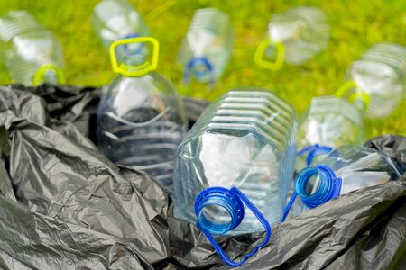 Plastic bottles in a black plastic trash bag on a grass background.の写真素材