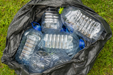 Plastic bottles in a black plastic trash bag on a grass background.の写真素材
