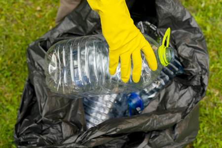 Hand putting empty plastic bottle into a black plastic trash bag.の写真素材