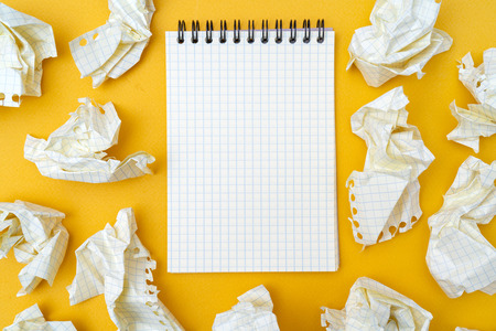 Notepad and crumpled sheets of paper on a yellow background.の写真素材