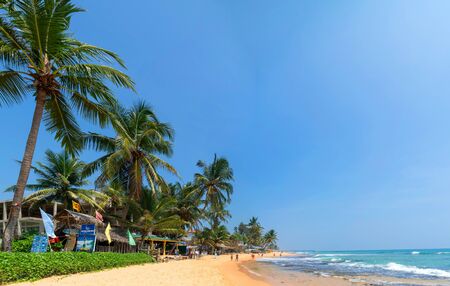 Hikkaduwa, Sri Lanka. March 6, 2018. Sunny Beach on Indian Ocean. Palm trees on sandy shore. People on coast.のeditorial素材