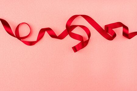 Red wavy ribbon on pink background. Holiday decoration. Valentine's Day decoration congratulation frame.の写真素材