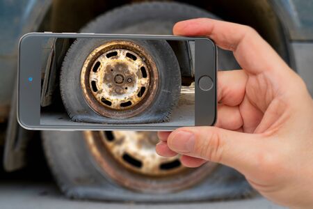 Flat tire old car. Photo smartphone. Smartphone in hand. Car wheel in the monitor.の写真素材