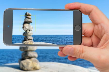 Stacked Rocks balancing, stacking with precision. Stone tower on shore. Photo smartphone. Smartphone...